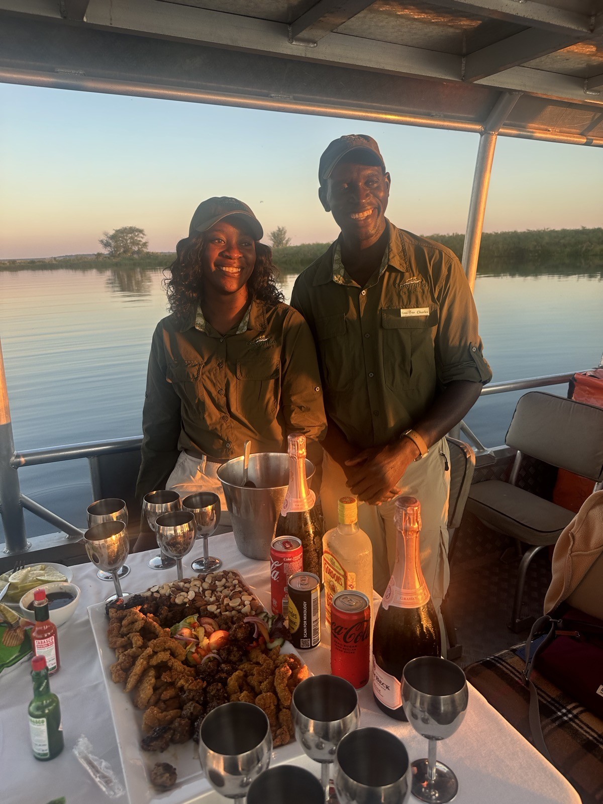 Two smiling CroisiAfrica safari guides with the sundowner spread on the boat at golden hour